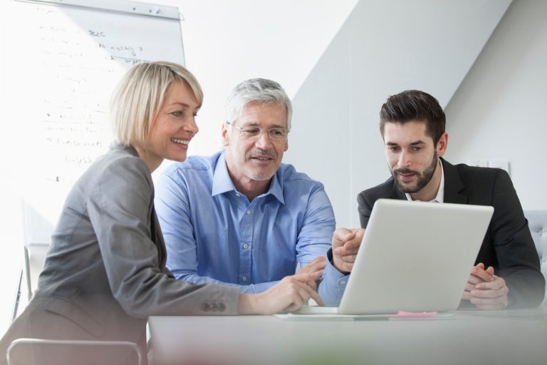 Trois personnes discutent devant un ordinateur portable en milieu professionnel.