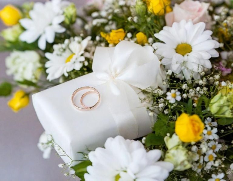Cadeau blanc avec une bague en or, entouré de fleurs colorées.