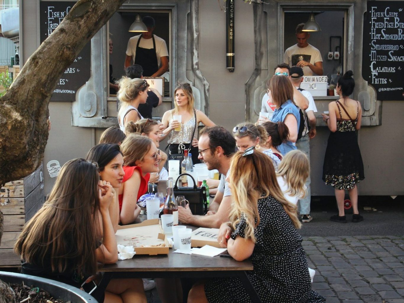 Groupe de personnes discutant autour d'une table, devant des fenêtres de restauration.