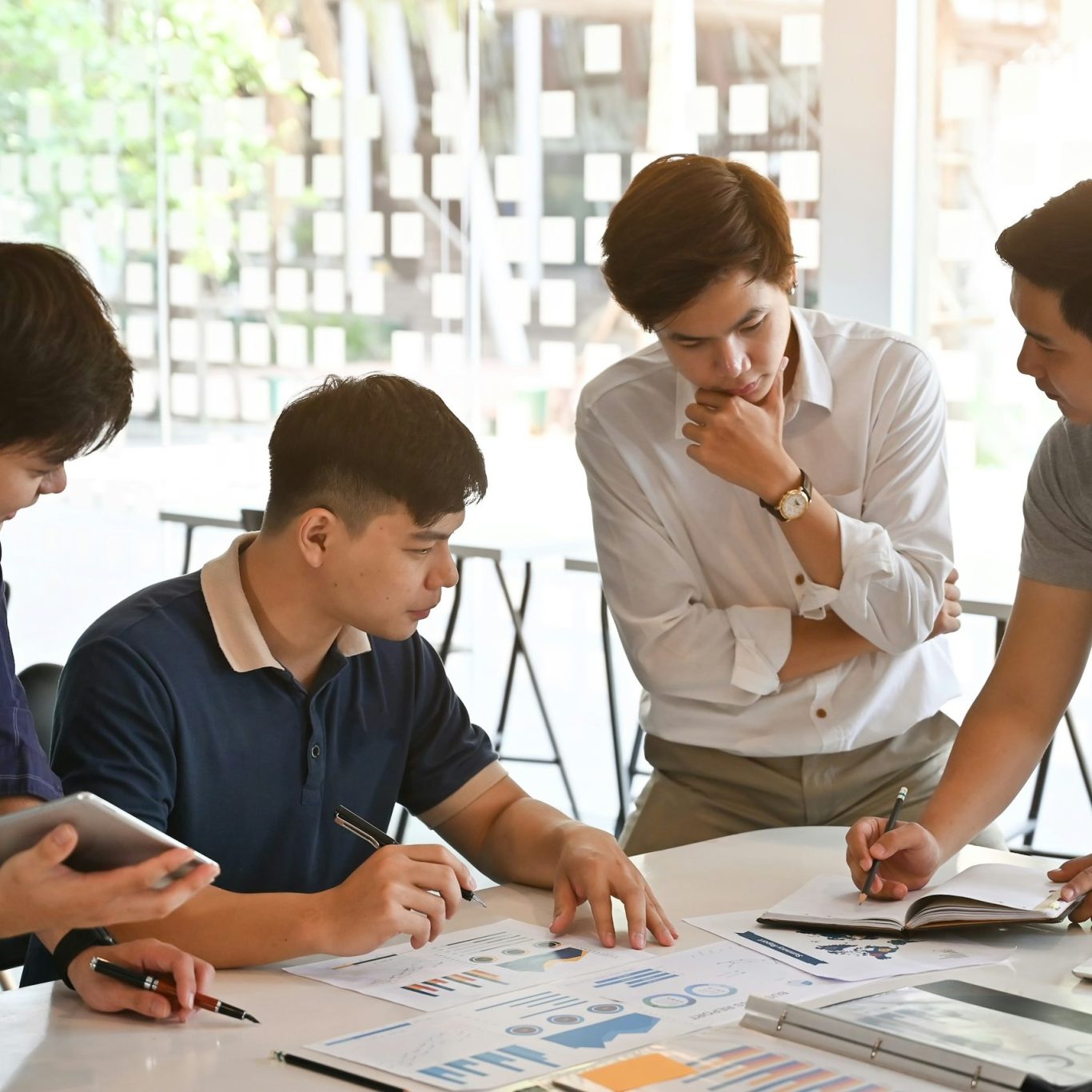 Quatre personnes collaborent autour d'une table, discutant de documents et de graphiques.