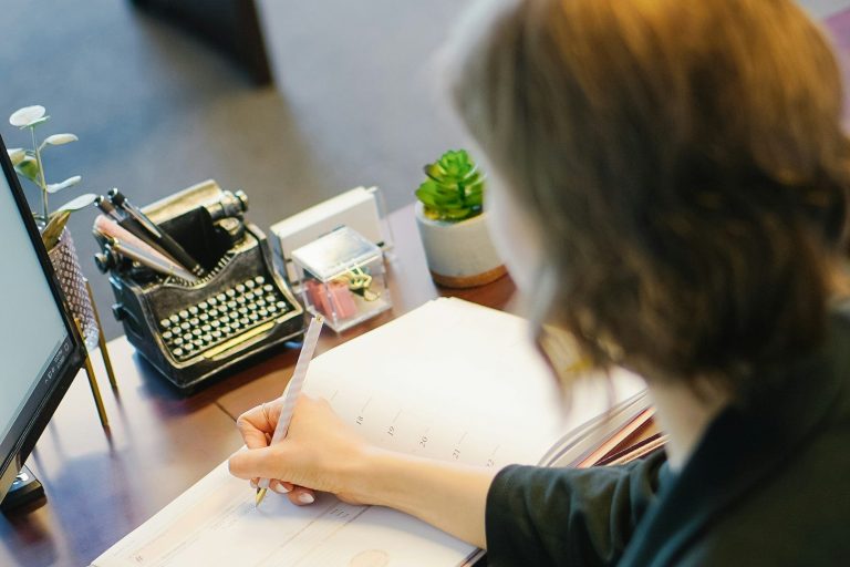 Femme écrivant à un bureau, avec une machine à écrire et une plante en pot.