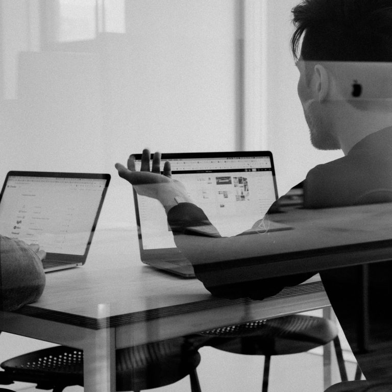 Un homme de dos, utilisant un ordinateur portable avec un autre à côté sur une table.