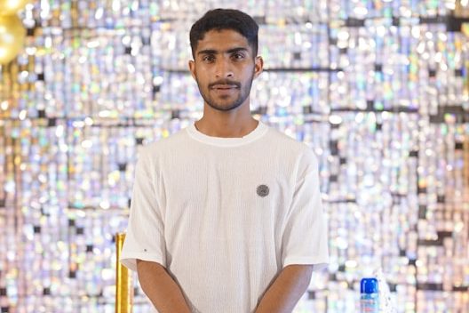 Homme en tee-shirt blanc devant un fond scintillant.