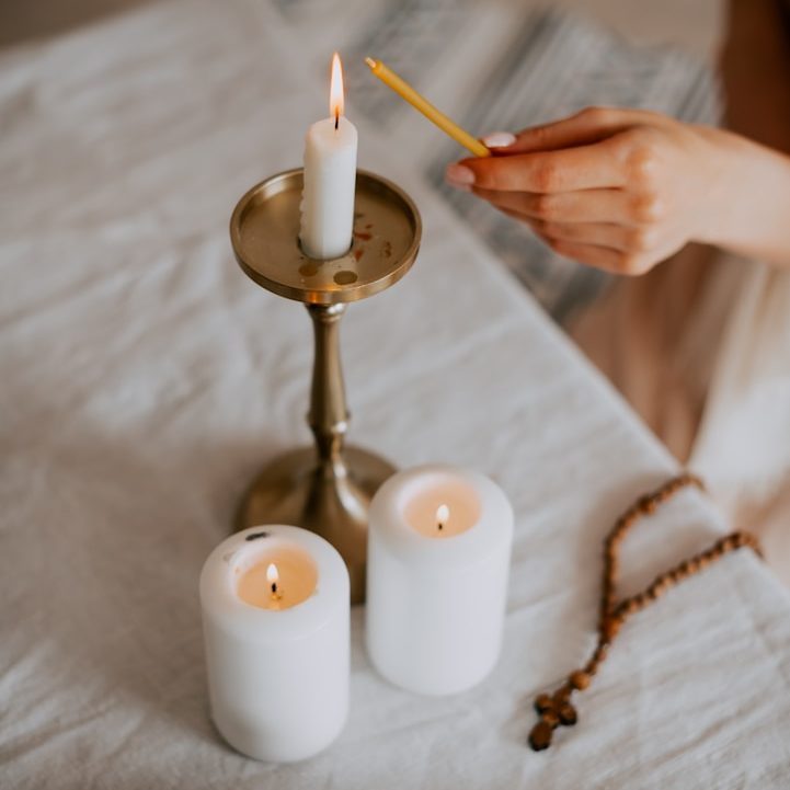 Bougie allumée sur un support avec deux bougies blanches et un chapelet en bois.