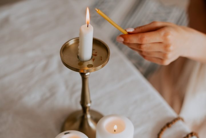 Main d'une personne allumant une bougie sur un porte-bougie doré. Tables décorées.